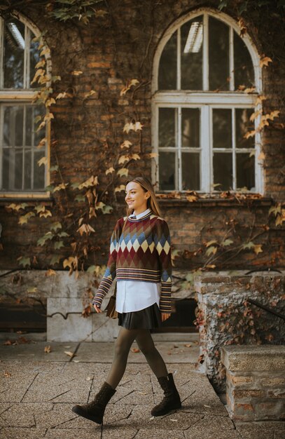 A street style shot of a person in the US wearing a fall layered outfit that includes a flannel shirt, a sweater vest, and a wool coat. The outfit is complemented by boots and a beanie.