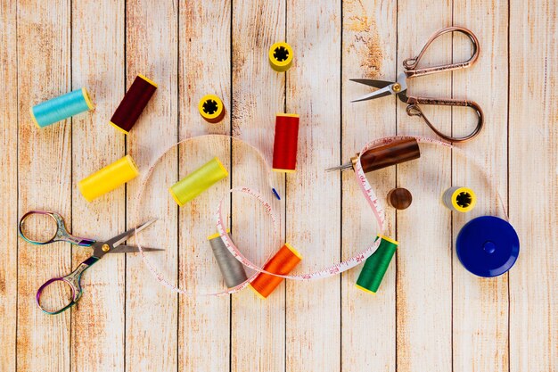 An organized sewing kit displayed on a wooden table, containing needles, thread spools in various colors, scissors, buttons, and a measuring tape.