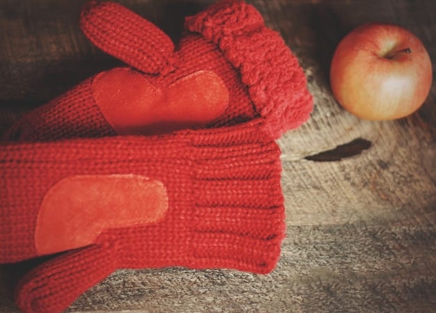 A close-up shot of various winter accessories such as knitted hats, gloves, and a scarf, arranged on a wooden table with a snowy background. The accessories are in different colors and textures.