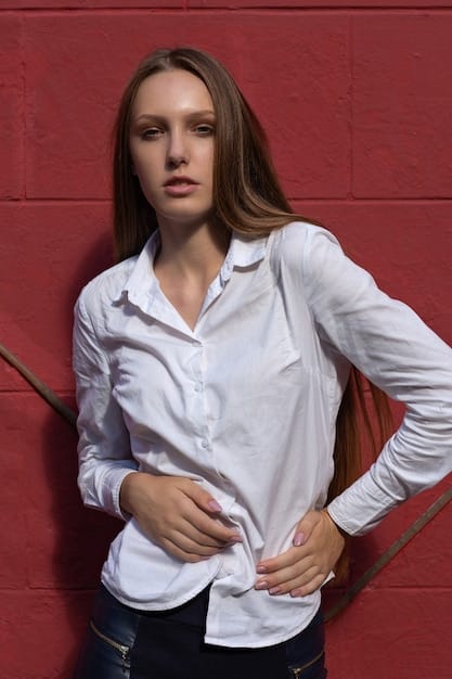 A close-up shot of a woman's torso wearing a crisp white shirt tucked into high-waisted, light-wash denim jeans, cinched with a brown leather belt. Her hands are casually placed in her pockets, highlighting the effortless and chic casual style.