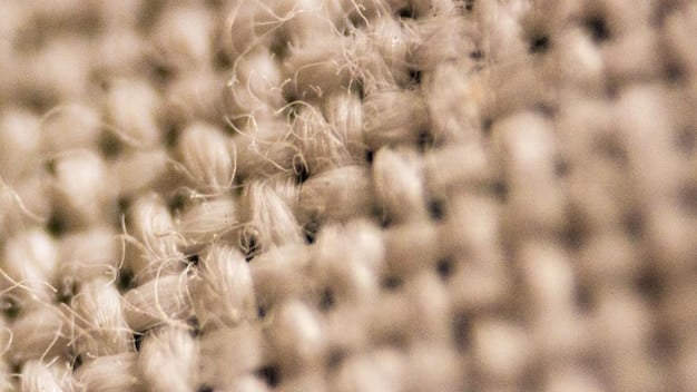 A close-up shot of linen fabric showing its texture and weave. Focus on the natural fibers and the way light passes through the material.