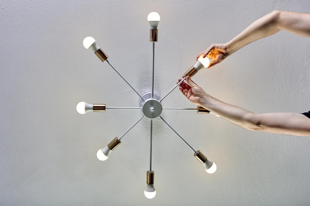 A close-up shot of a smart bulb being installed in a modern ceiling fixture. The bulb is partially screwed in, revealing its internal components. The background is slightly blurred to emphasize the bulb and the act of installation.