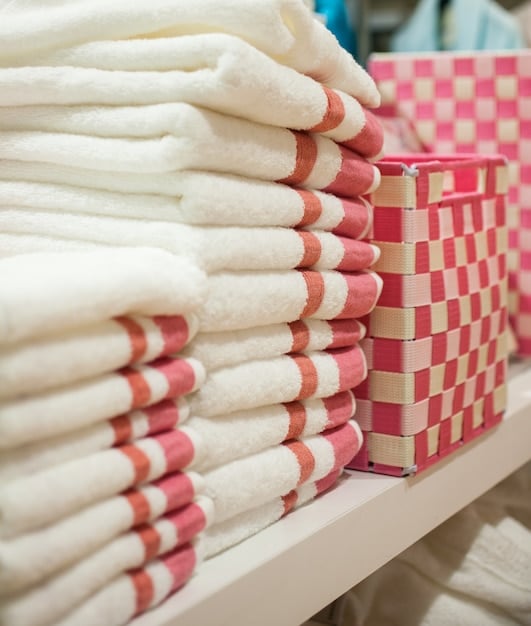 A meticulously organized linen closet with neatly rolled towels, folded sheet sets, and labeled baskets containing toiletries and other household supplies, all arranged in a visually appealing and easily accessible manner.