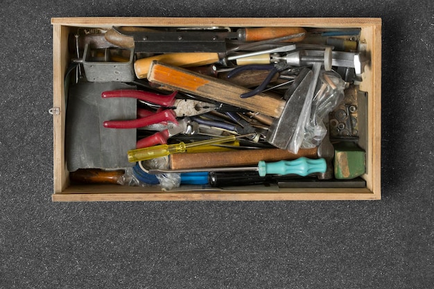 A well-organized toolbox is opened, revealing a variety of essential tools neatly arranged inside. Tools such as a hammer, screwdrivers, pliers, wrench, measuring tape, level, and utility knife are clearly visible. The backdrop should show a home workspace with tools hanging on the wall.