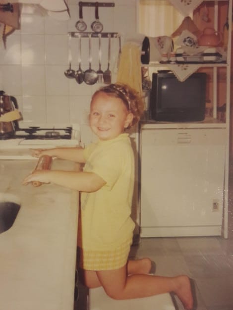 Close up shot of a clear, adhesive child safety lock on a kitchen cabinet, preventing a child from opening it. The background shows blurred kitchen utensils and dishes.