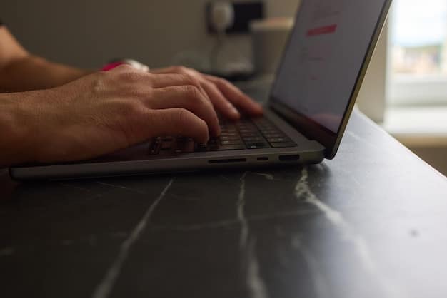 A close-up of a person's hands typing on a MacBook Pro keyboard. The focus is on the keyboard and trackpad, highlighting the sleek design and ergonomic features. The background is blurred with a coffee cup and some notebooks, suggesting a productive work environment.
