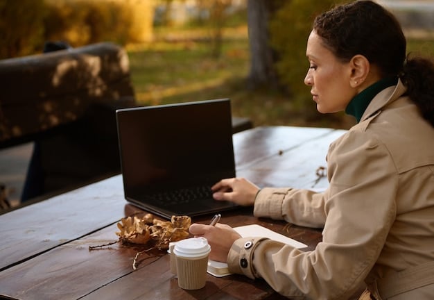 A person working on a laptop outdoors at a cafe. The laptop has an anti-glare screen, making it easy to see even in bright sunlight. The cafe setting includes coffee cups, pastries, and other people in the background.